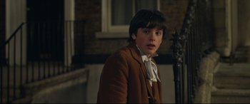 Movie still from “Sing Street” (2016), directed by John Carney – A young man in a brown jacket and a white bow tie; Close Up shot, Over the shoulder angle