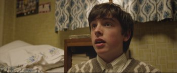 Movie still from “Sing Street” (2016), directed by John Carney – A young man in a sweater and tie looking at the camera; Close Up shot, Over the shoulder angle