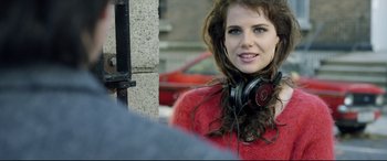 Movie still from “Sing Street” (2016), directed by John Carney – A beautiful young lady wearing headphones and posing for a picture; Close Up shot, Over the shoulder angle