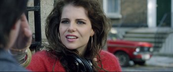Movie still from “Sing Street” (2016), directed by John Carney – A woman wearing a red jacket and black headphones; Close Up shot, Over the shoulder angle