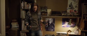 Movie still from “Sing Street” (2016), directed by John Carney – A man holding a pair of scissors in his hands; Medium shot, Over the shoulder angle