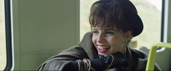 Movie still from “Sing Street” (2016), directed by John Carney – A young woman smiles brightly while sitting in front of a window; Close Up shot, Over the shoulder angle