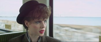 Movie still from “Sing Street” (2016), directed by John Carney – A person wearing a hat near a window; Close Up shot, Over the shoulder angle