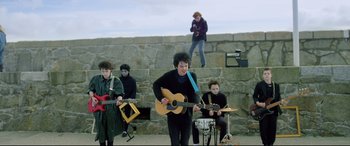 Movie still from “Sing Street” (2016), directed by John Carney – A group of young people playing instruments on a stage; Wide shot, High angle