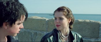 Movie still from “Sing Street” (2016), directed by John Carney – A young woman wearing a black jacket and pearls; Close Up shot, Over the shoulder angle
