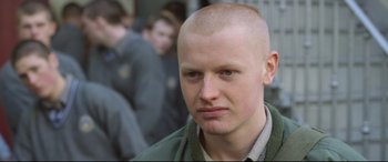 Movie still from “Sing Street” (2016), directed by John Carney – A man with a shaved head is standing in front of a group of people; Close Up shot, High angle