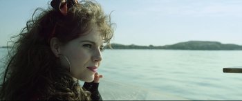Movie still from “Sing Street” (2016), directed by John Carney – A beautiful young lady sitting on top of a boat in the water; Close Up shot, Low angle