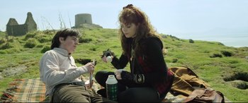 Movie still from “Sing Street” (2016), directed by John Carney – A woman sitting on the ground next to a man; Medium shot, Over the shoulder angle