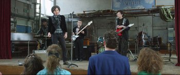 Movie still from “Sing Street” (2016), directed by John Carney – A group of young people playing music in front of a crowd; Wide shot, Over the shoulder angle