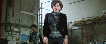 Movie still from “Sing Street” (2016), directed by John Carney – A young man wearing a hat singing into a microphone; Medium shot, Over the shoulder angle