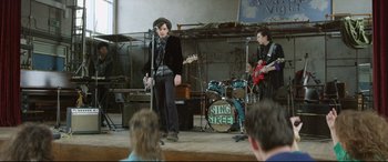 Movie still from “Sing Street” (2016), directed by John Carney – A group of young people performing on a stage; Wide shot, Over the shoulder angle