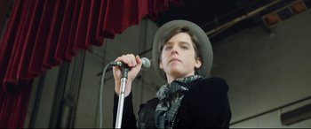 Movie still from “Sing Street” (2016), directed by John Carney – A person holding a microphone and wearing a hat; Close Up shot, Low angle