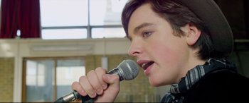Movie still from “Sing Street” (2016), directed by John Carney – A person holding a microphone up to their mouth; Close Up shot, Low angle