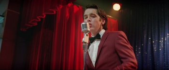 Movie still from “Sing Street” (2016), directed by John Carney – A man in a red suit is singing into a microphone; Medium shot, Low angle