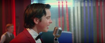 Movie still from “Sing Street” (2016), directed by John Carney – A young man is singing into a microphone; Close Up shot, Over the shoulder angle
