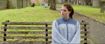 Movie still from “Sing Street” (2016), directed by John Carney – A woman sitting on top of a wooden park bench; Medium shot, Over the shoulder angle