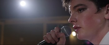 Movie still from “Sing Street” (2016), directed by John Carney – A man holding a microphone up to his mouth; Extreme Close Up shot, Low angle