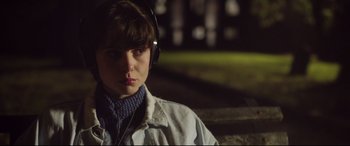 Movie still from “Sing Street” (2016), directed by John Carney – A person wearing headphones and a white jacket; Close Up shot, Over the shoulder angle