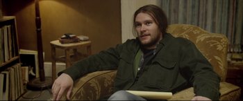 Movie still from “Sing Street” (2016), directed by John Carney – A man sitting in a chair holding a paper; Close Up shot, Over the shoulder angle
