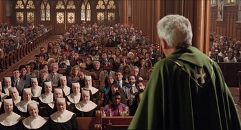 Movie still from “Sister Act” (1992), directed by Emile Ardolino – A large group of people sitting in front of a priest; Wide shot, High angle