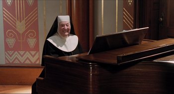 Movie still from “Sister Act” (1992), directed by Emile Ardolino – A nun sitting at a piano smiling for the camera; Medium shot, High angle