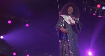 Movie still from “Sister Act 2: Back in the Habit” (1993), directed by Bill Duke – A woman in a long dress is holding a microphone; Medium shot, Low angle