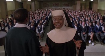 Movie still from “Sister Act 2: Back in the Habit” (1993), directed by Bill Duke – A nun is smiling in front of a large group of people; Medium shot, Low angle
