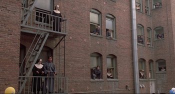 Movie still from “Sister Act 2: Back in the Habit” (1993), directed by Bill Duke – A group of people standing on fire escape of a brick building; Extreme Wide shot, High angle