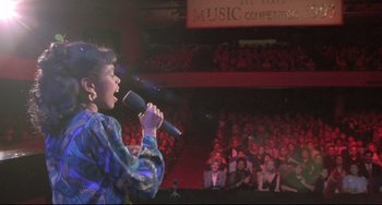 Movie still from “Sister Act 2: Back in the Habit” (1993), directed by Bill Duke – A woman holding a microphone while standing in front of an audience; Medium shot, High angle