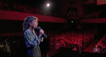 Movie still from “Sister Act 2: Back in the Habit” (1993), directed by Bill Duke – A woman holding a microphone while standing in front of an audience; Medium shot, High angle