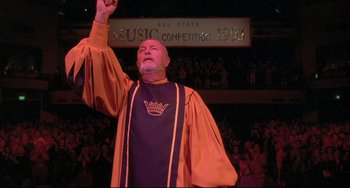 Movie still from “Sister Act 2: Back in the Habit” (1993), directed by Bill Duke – A man in a purple and orange robe raising his fist; Medium shot, Low angle