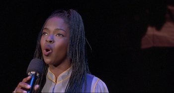Movie still from “Sister Act 2: Back in the Habit” (1993), directed by Bill Duke – A woman with long braids is singing into a microphone; Close Up shot, Low angle