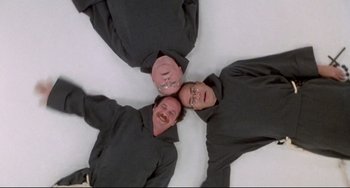Movie still from “Sister Act 2: Back in the Habit” (1993), directed by Bill Duke – A group of men laying on the ground with their heads together; Wide shot, Overhead angle