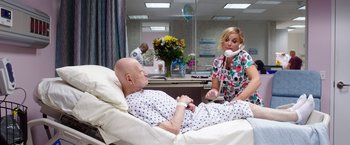 Movie still from “Sisters” (2015), directed by Jason Moore – A woman talking on a phone while a man lies in a hospital bed; Medium shot, High angle