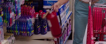 Movie still from “Sisters” (2015), directed by Jason Moore – A person holding a fire extinguisher next to a shelf; Medium shot, High angle