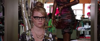 Movie still from “Sisters” (2015), directed by Jason Moore – A woman wearing glasses and a bun in front of a mannequin; Close Up shot, Over the shoulder angle