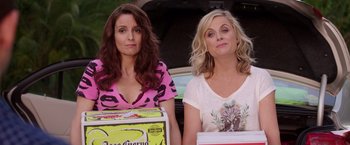 Movie still from “Sisters” (2015), directed by Jason Moore – Two women sitting next to each other in front of an open trunk of a car; Medium shot, High angle