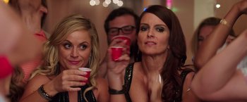 Movie still from “Sisters” (2015), directed by Jason Moore – Two women and a man are holding drinks; Close Up shot, Over the shoulder angle