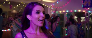 Movie still from “Sisters” (2015), directed by Jason Moore – A beautiful woman smiling at the camera in front of a group of people; Close Up shot, Over the shoulder angle