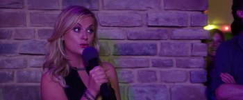 Movie still from “Sisters” (2015), directed by Jason Moore – A woman holding a microphone in front of a brick wall; Close Up shot, Over the shoulder angle