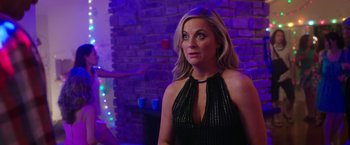 Movie still from “Sisters” (2015), directed by Jason Moore – A woman in a black dress is standing in front of a brick wall; Medium shot, Over the shoulder angle