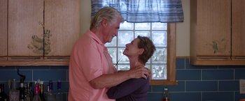 Movie still from “Sisters” (2015), directed by Jason Moore – An older man and a younger woman embracing in front of a window; Medium shot, Over the shoulder angle