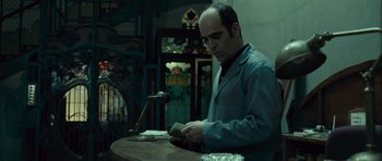 Movie still from “Sleep Tight” (2011), directed by Jaume Balagueró – A man sitting in front of a microphone at a table; Medium shot, Low angle