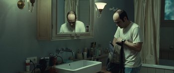 Movie still from “Sleep Tight” (2011), directed by Jaume Balagueró – A man with a bald head in a bathroom; Medium shot, Over the shoulder angle