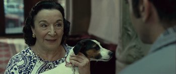 Movie still from “Sleep Tight” (2011), directed by Jaume Balagueró – An older woman holding a brown and white dog; Close Up shot, Over the shoulder angle