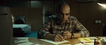 Movie still from “Sleep Tight” (2011), directed by Jaume Balagueró – A man sitting at a table writing on a piece of paper; Close Up shot, Over the shoulder angle