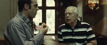 Movie still from “Sleep Tight” (2011), directed by Jaume Balagueró – A man and an older man sitting at a table; Medium shot, Over the shoulder angle