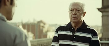 Movie still from “Sleep Tight” (2011), directed by Jaume Balagueró – An older man in a striped polo shirt looks into the distance; Close Up shot, Low angle