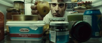 Movie still from “Sleep Tight” (2011), directed by Jaume Balagueró – A man holding an apple in front of jars of food; Extreme Close Up shot, Overhead angle
