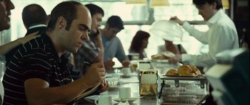 Movie still from “Sleep Tight” (2011), directed by Jaume Balagueró – A group of people sitting at a table with cups of coffee; Medium shot, Over the shoulder angle
